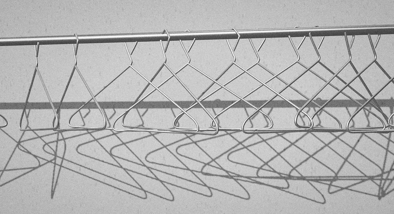 Black-and-white photograph of empty wire hangers on a rail casting sharp shadows on a wall.