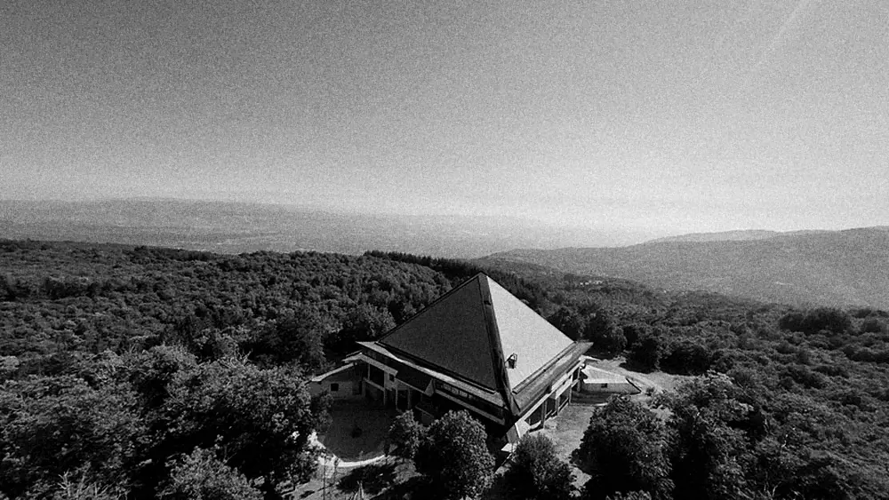 Black-and-white photograph of the base's pyramid roof rising out of dense woods, with hills behind.